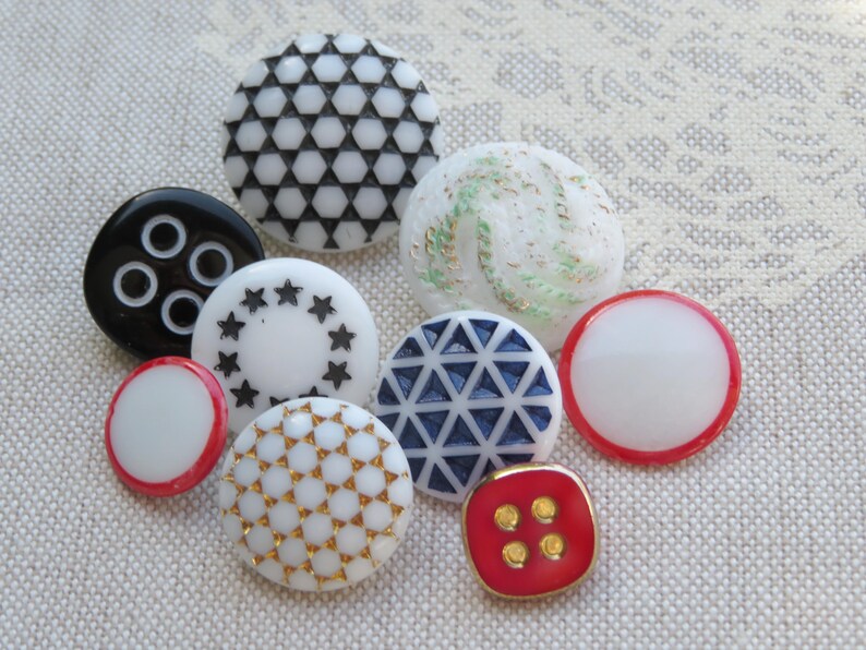 May include: Assortment of colorful buttons with various patterns and designs, including black and white geometric, white with gold accents, white with black stars, white with red trim, and red with gold accents.