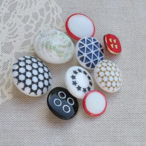 May include: Assortment of vintage buttons in various colors and patterns, including white, black, red, blue, and gold. The buttons feature geometric designs, stars, and dots.