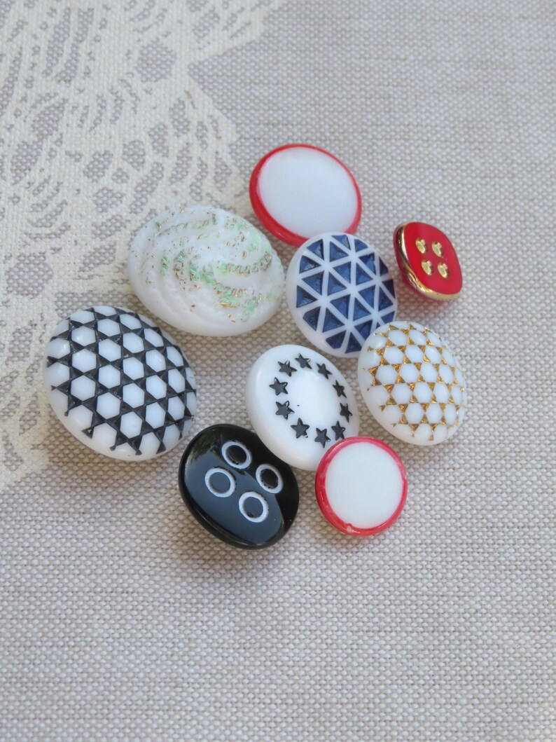 May include: Assortment of vintage buttons in various colors and patterns, including white, black, red, blue, and gold. The buttons feature geometric designs, stars, and dots.