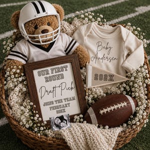 Puede incluir: Un oso de peluche marrón con casco y camiseta de fútbol americano, un body de bebé color crema de manga larga con Baby Andersen, un marco con Our First Round Draft Pick Joins The Team February 202X, un banderín 202X y un balón de fútbol.