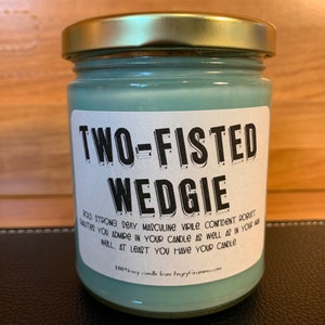 K&ouml;nnte beinhalten: Eine tealfarbene Glaskerze in einem Glas mit einem wei&szlig;en Etikett, auf dem "TWO-FISTED WEDGIE" steht, und einer humorvollen Beschreibung der Eigenschaften, die Sie an Ihrer Kerze sch&auml;tzen. Die Kerze ist 100% Soja.