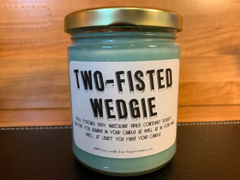 K&ouml;nnte beinhalten: Eine tealfarbene Glaskerze in einem Glas mit einem wei&szlig;en Etikett, auf dem "TWO-FISTED WEDGIE" steht, und einer humorvollen Beschreibung der Eigenschaften, die Sie an Ihrer Kerze sch&auml;tzen. Die Kerze ist 100% Soja.
