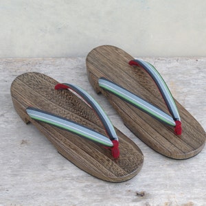 May include: A pair of wooden geta sandals with red, green, and gray striped straps. The sandals are made of dark brown wood and have a traditional Japanese design.