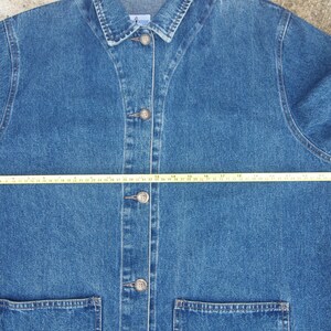 May include: A blue denim jacket with a button closure and two front pockets. The jacket is measured across the chest with a tape measure, showing a measurement of 24 inches.