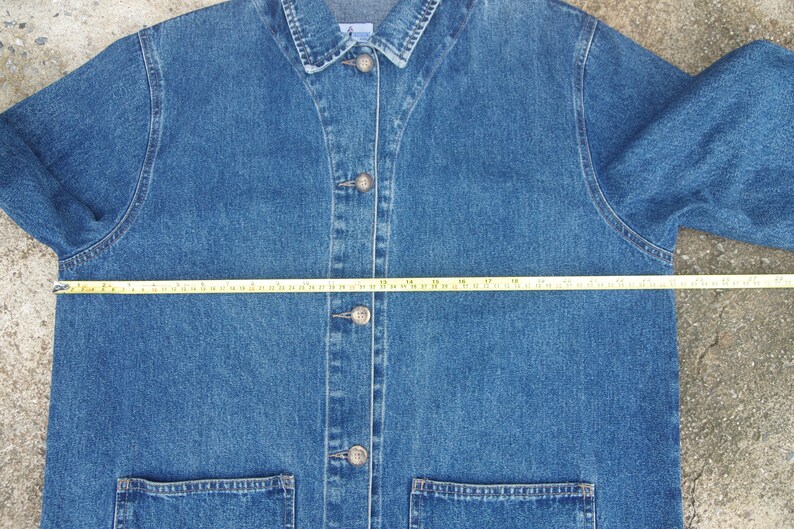 May include: A blue denim jacket with a button closure and two front pockets. The jacket is measured across the chest with a tape measure, showing a measurement of 24 inches.