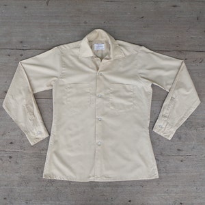 May include: A light beige long-sleeved button-down shirt with two chest pockets.