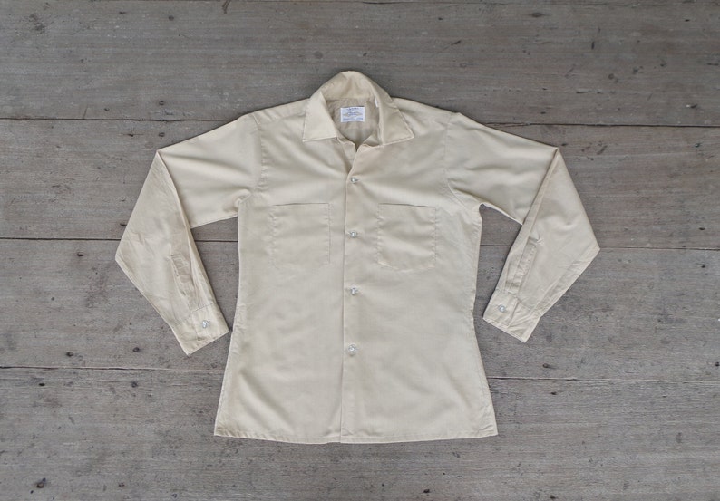 May include: A light beige long-sleeved button-down shirt with two chest pockets.