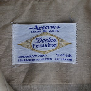 May include: A white tag with blue text that reads "Arrow> Made in U.S.A. Decton Permafron Sanforized-Plus S-14-14 1/2 65% Dacron Polyester-35% Cotton"