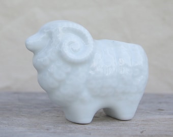 May include: A white ceramic ram figurine with a curled horn. The figurine is a simple, minimalist design.