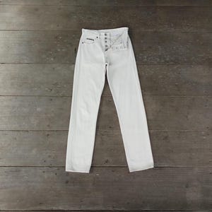 Puede incluir: Una taza de cerámica blanca con un asa negra y el texto "But First, Coffee" en negro, con una fuente de estilo manuscrito. La taza está sobre una superficie blanca.