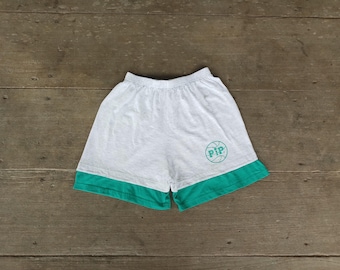 May include: Gray athletic shorts with a teal green hem. The shorts have an elastic waistband and a teal green graphic of a basketball with the letters "PIP" inside. The shorts are made of a soft, lightweight material.