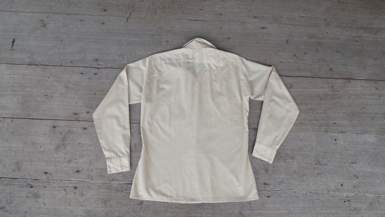 May include: A long-sleeved, light cream colored button-down shirt with a collar.
