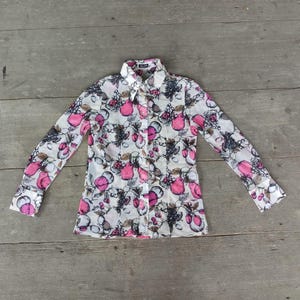 May include: A white long-sleeved shirt with a pink and black floral print. The shirt has a button-up front and a collar.