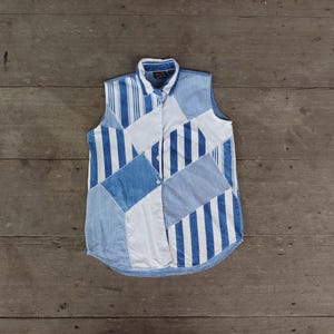 May include: A sleeveless button-up shirt made of patchwork denim in shades of blue and white. The shirt has a geometric pattern with stripes and squares.