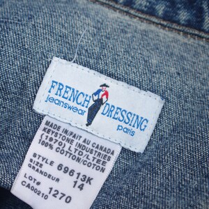 May include: White tag with blue text and a small illustration of a person wearing a cowboy hat. The tag reads "French Dressing Jeanswear Paris" and includes the text "Made in/Fait au Canada Keystone Industries (1970) Ltd/Ltee 100% Cotton/Coton Style 69613K Grandeur 14 Lot # 1270 CA00210".