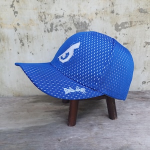 May include: A blue baseball cap with a white logo and the text "Bad Boy". The cap has a curved brim and a mesh design. The cap is sitting on a small wooden stool.