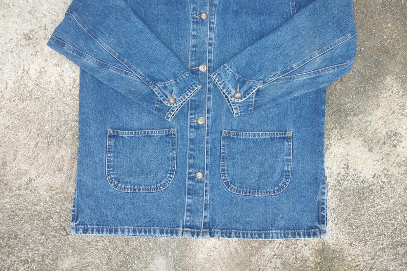 May include: A blue denim jacket with a button-up front and two large pockets on the front. The jacket has long sleeves with buttoned cuffs.