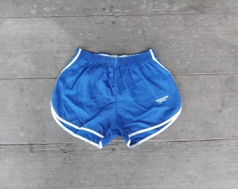 May include: Blue athletic shorts with white trim. The shorts have an elastic waistband and a small logo on the left leg. The shorts are made of a lightweight, possibly nylon, material.