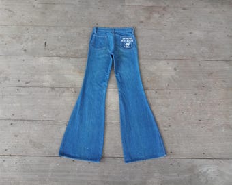 Puede incluir: Un par de pantalones vaqueros de campana azul de mezclilla con un parche blanco en el bolsillo trasero que dice "Wrangler".