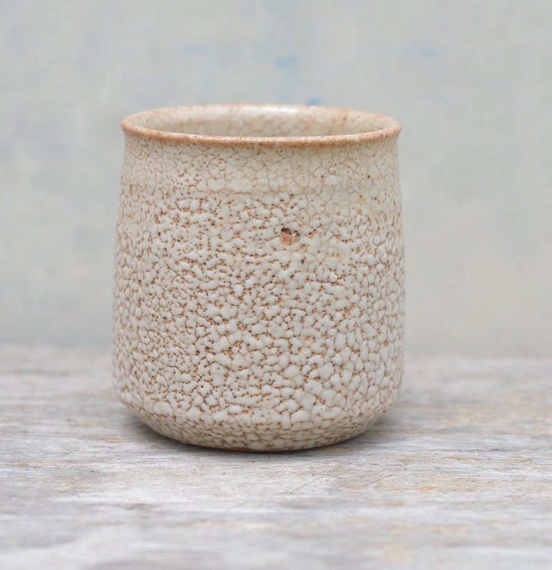 Puede incluir: Una taza de cer&aacute;mica blanca con una superficie texturizada y moteada. La taza tiene una forma redondeada y un labio ligeramente acampanado.