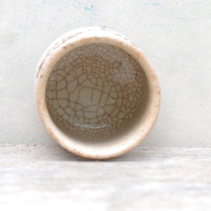 Puede incluir: Una taza peque&ntilde;a de cer&aacute;mica blanca con un esmalte craquelado. La taza est&aacute; vac&iacute;a y tiene un borde marr&oacute;n.