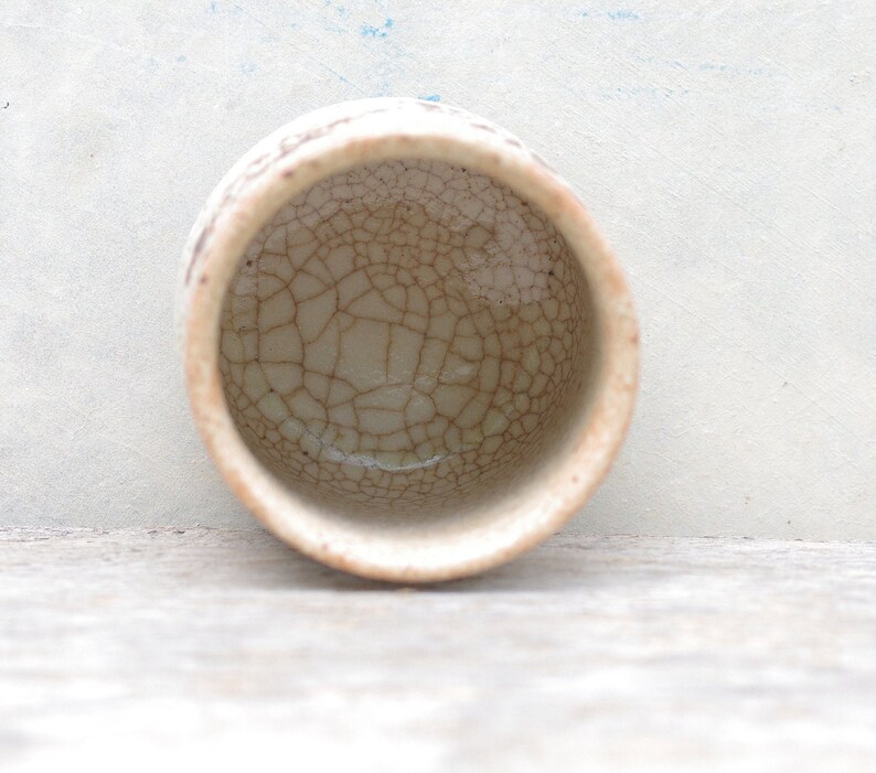 Puede incluir: Una taza peque&ntilde;a de cer&aacute;mica blanca con un esmalte craquelado. La taza est&aacute; vac&iacute;a y tiene un borde marr&oacute;n.