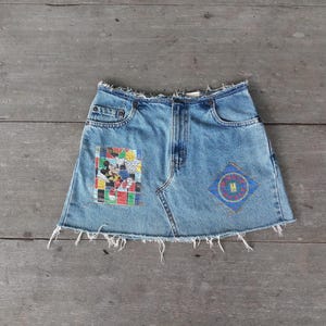 May include: A blue denim skirt with frayed edges and two patches. One patch features a cartoon image of Mickey Mouse and Minnie Mouse. The other patch has a circular design with the text "Minnie Mouse" inside.