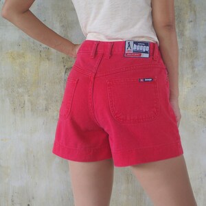 Puede incluir: Pantalones cortos de mezclilla rojos de cintura alta con un bolsillo trasero. Los pantalones cortos tienen una etiqueta de la marca "Bongo" en la parte posterior.