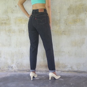 Puede incluir: Un par de pantalones vaqueros de mezclilla de lavado oscuro con cintura alta y pierna recta. Los vaqueros tienen un diseño clásico de cinco bolsillos y un parche de cuero en la parte posterior de la cintura con el logotipo de Levi's.