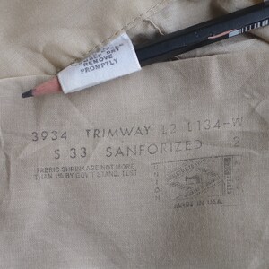 May include: A close-up of a beige fabric label with the text "3934 TRIMWAY 12 1134-W S 33 SANFORIZED 2" and "FABRIC SHRINKAGE NOT MORE THAN 1% BY GOV'T STAND TEST MADE IN USA".