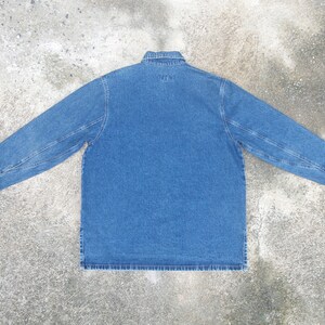 May include: A blue denim shirt with a button-up collar and long sleeves. The shirt has a single pocket on the left chest and the text "WTW" is embroidered on the back.