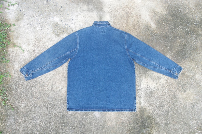 May include: A blue denim shirt with a button-up collar and long sleeves. The shirt has a single pocket on the left chest and the text "WTW" is embroidered on the back.