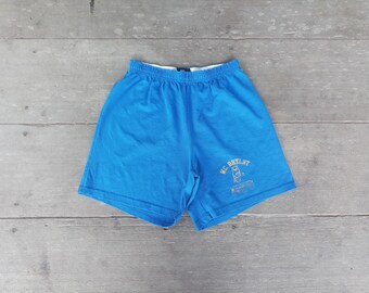 May include: Bright blue athletic shorts with an elastic waistband. The shorts feature the text "MC BRYANT" in a gold color, along with a graphic. The shorts are made of a lightweight material and are suitable for sports or casual wear.