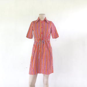 May include: A vintage red, yellow, and white striped dress with short sleeves and a collared neckline. The dress features a drawstring waist and red buttons down the front. The dress is displayed on a mannequin.