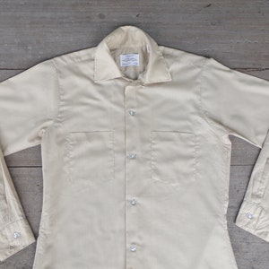 May include: A light yellow long-sleeved button-down shirt with two chest pockets.
