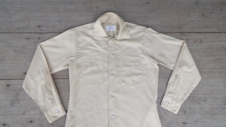 May include: A light yellow long-sleeved button-down shirt with two chest pockets.