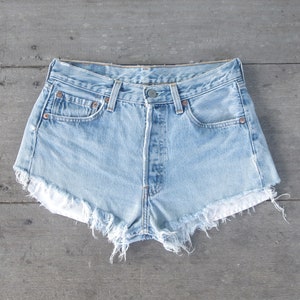 May include: Light blue denim shorts with frayed edges. The shorts have a button fly and five pockets.