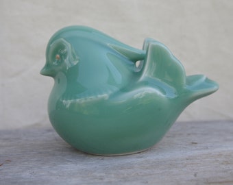May include: A teal ceramic bird figurine with a glossy finish. The bird has a rounded body, a small beak, and a curved tail. The figurine is a decorative item, likely for display.