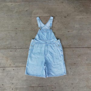 Pode incluir: Macacão de ganga azul claro com alças ajustáveis e um caimento descontraído. O macacão tem um design clássico com dois bolsos frontais e dois bolsos traseiros.