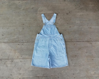 Puede incluir: Pantalón vaquero azul claro con tirantes ajustables y un corte holgado. El pantalón tiene un diseño clásico con dos bolsillos delanteros y dos bolsillos traseros.
