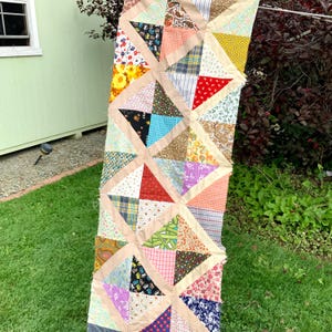 May include: A long, rectangular patchwork quilt with a geometric pattern of triangles and squares. The quilt is made of various fabrics in a variety of colors, including red, blue, green, yellow, and brown.