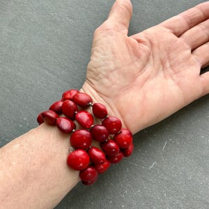 Puede incluir: Una vibrante pulsera de cuentas rojas con un diseño de múltiples hilos. La pulsera presenta cuentas grandes y redondas con un acabado brillante. Las cuentas están ensartadas con conectores plateados, creando un accesorio llamativo.