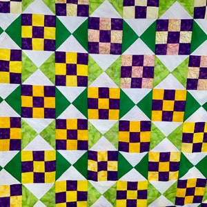 Może przedstawiać: Kołdra w kratkę w odcieniach żółtego, fioletowego i zielonego. Kołdra składa się z kwadratów z kratką w środku i zielonymi trójkątami w rogach.