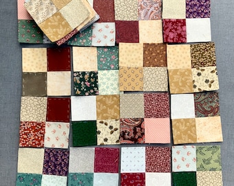 Può includere: Un blocco di trapunta patchwork composto da 36 quadrati di tessuto in vari colori e motivi, tra cui verde, marrone, rosso, bianco e crema. I quadrati sono disposti in un motivo a griglia, con ogni quadrato di un colore o motivo diverso.