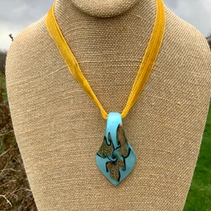 May include: A blue and gold glass pendant necklace with a swirl design, hanging from a yellow ribbon.