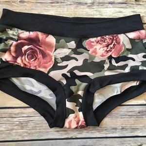 May include: Black and green underwear with a camouflage and floral print. The underwear has a black elastic waistband and trim.