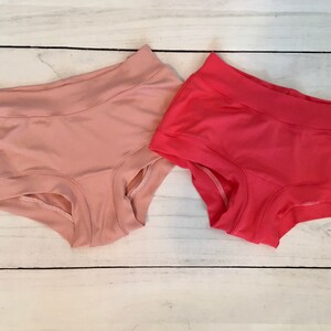 May include: Two pairs of underwear, one pink and one red, on a white wooden surface.