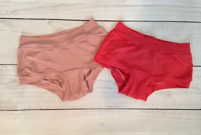May include: Two pairs of underwear, one pink and one red, on a white wooden surface.