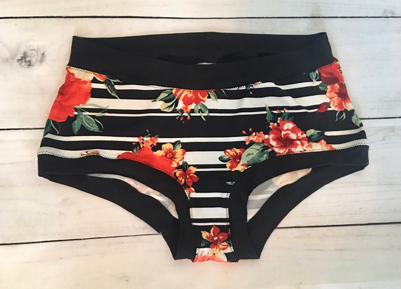 May include: Black and white striped underwear with a floral print featuring red, orange, and yellow flowers. The underwear has a black elastic waistband.