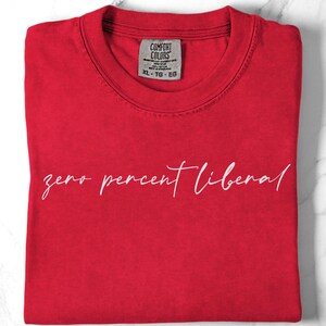 May include: A red Comfort Colors t-shirt with the text "zero percent liberal" in white script. The shirt is folded neatly, with the tag visible at the neckline. The XL-TG-EG tag is visible.